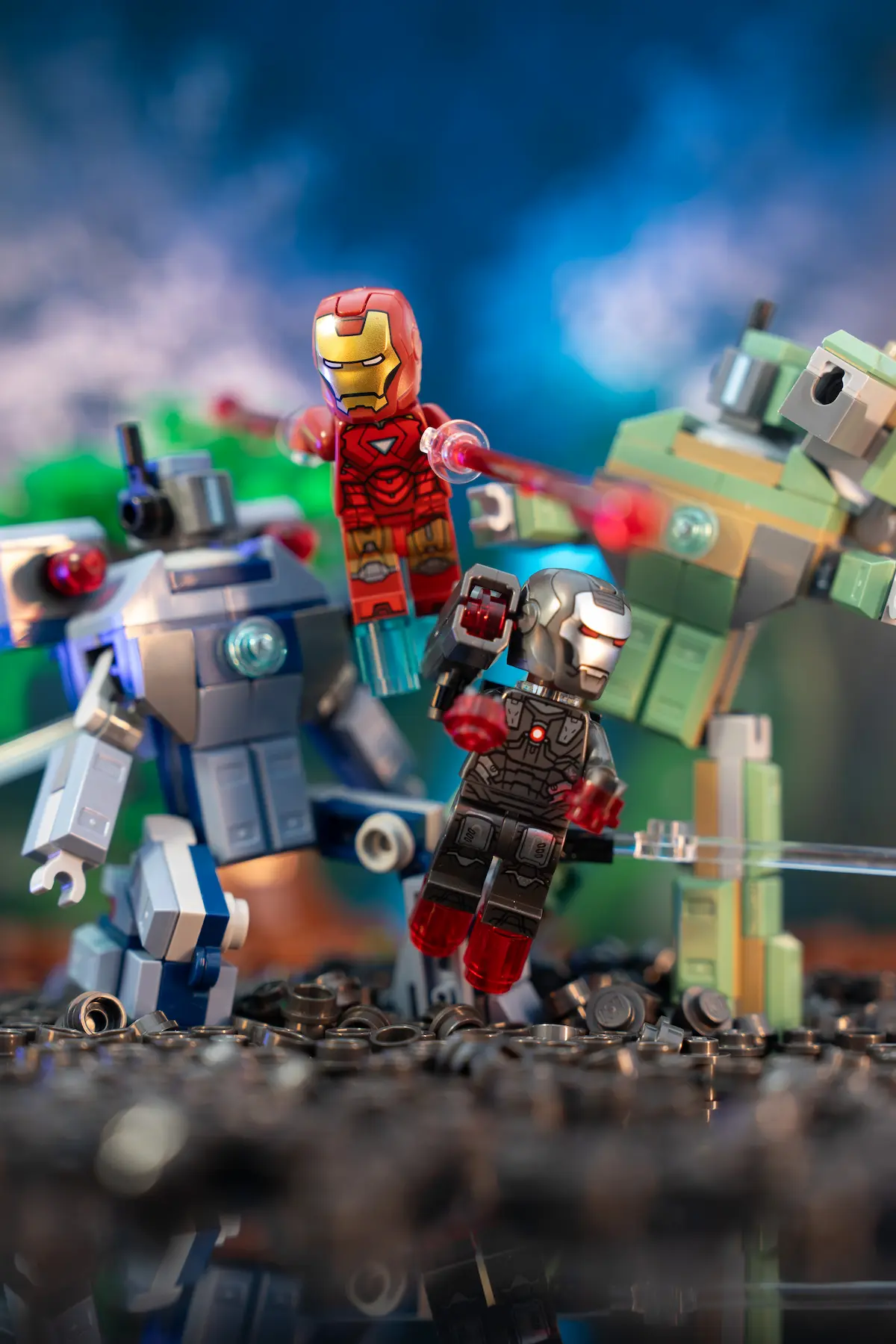 LEGO Iron Man and War Machine minifigures suspended mid-air in dynamic action poses, facing two large hammer droids on a rocky battlefield with dramatic lighting and a blurred blue-green background.