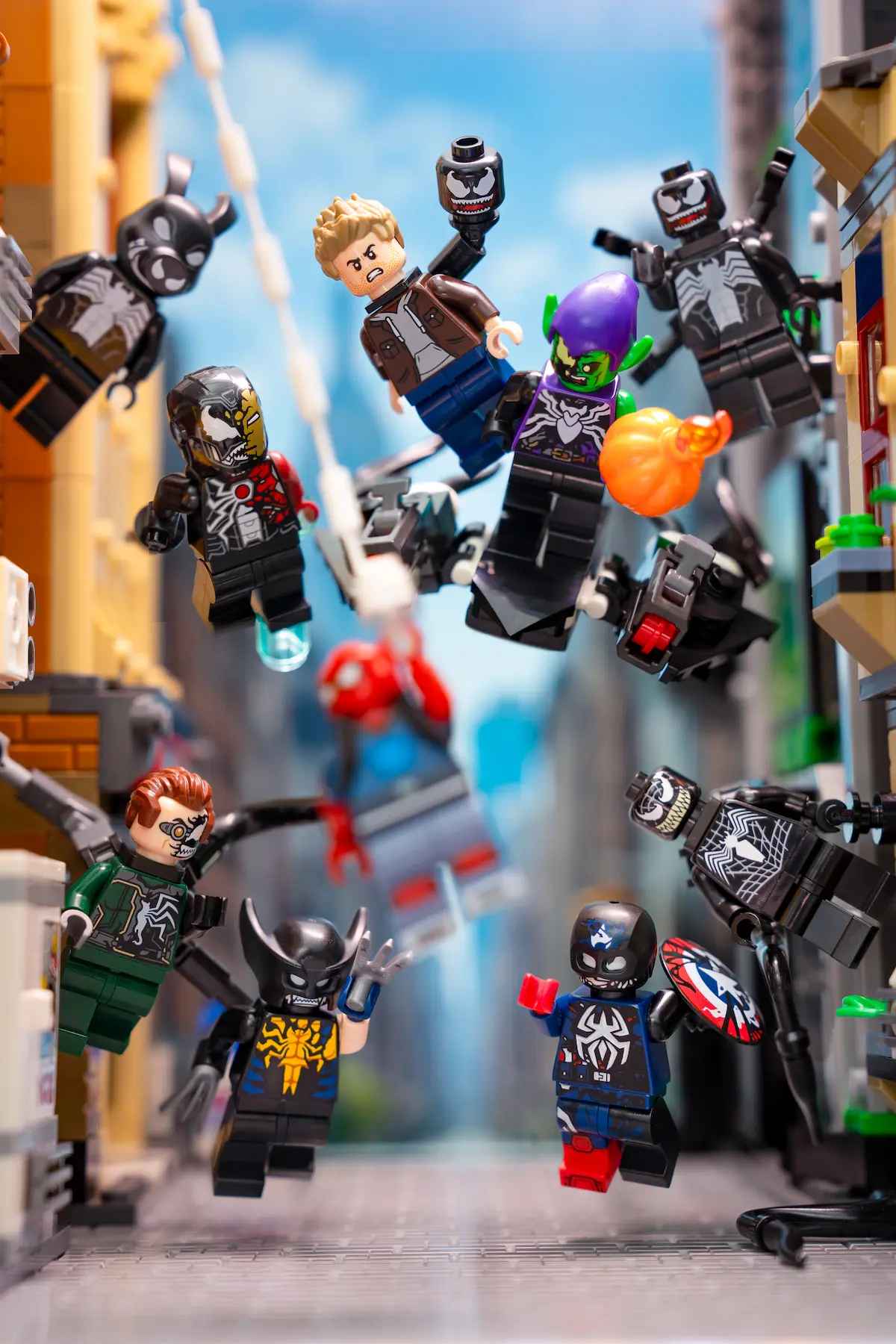 Multiple LEGO Marvel symbiote minifigures suspended mid-air in dynamic action poses, arranged across a city street scene with buildings on both sides and a bright blue sky in the background.