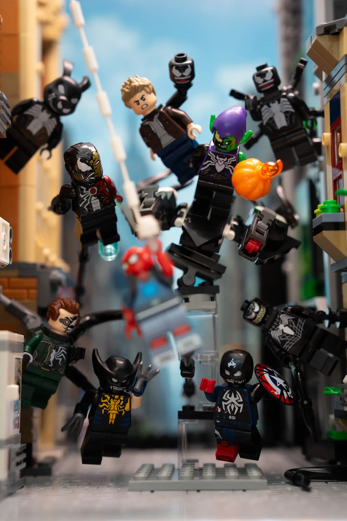 Multiple LEGO Marvel symbiote minifigures suspended mid-air in dynamic action poses, arranged across a city street scene with buildings on both sides and a bright blue sky in the background.