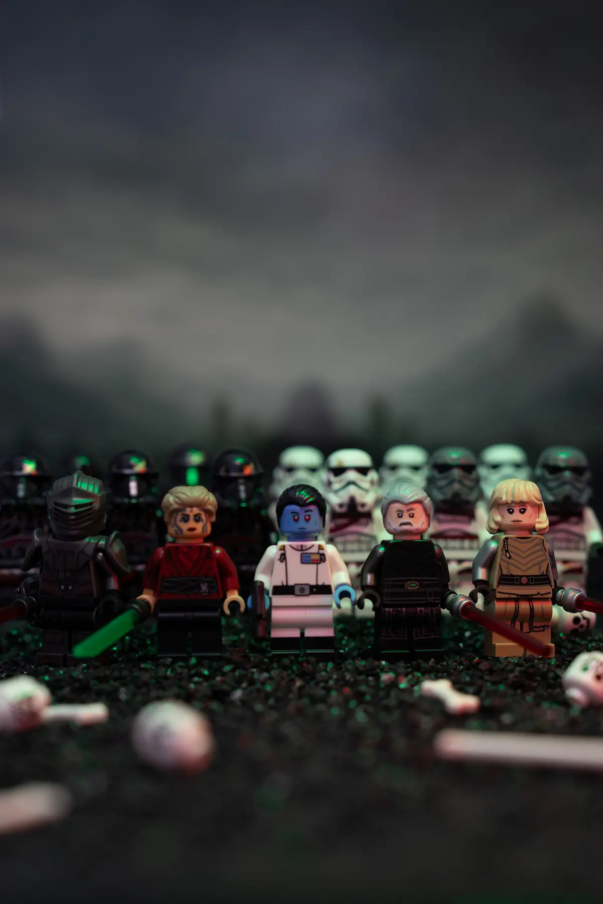 A lineup of LEGO Star Wars minifigures holding glowing red and green lightsabers, standing on a dark battlefield with stormtroopers blurred in the background under a moody, overcast sky.