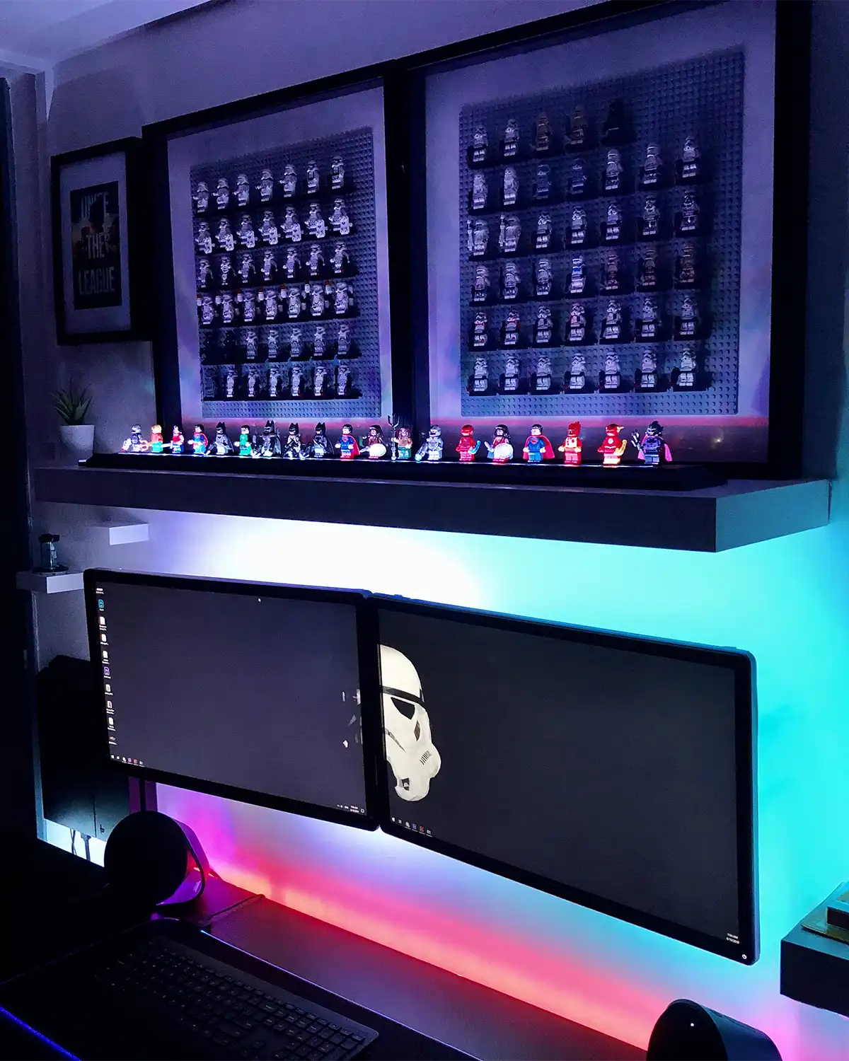 LEGO superhero minifigures displayed on LED-lit shelves, glowing in blue and white light. The setup features DC characters like Batman, Superman, and Wonder Woman, with framed minifigure displays and a LEGO Statue of Liberty build in the background.