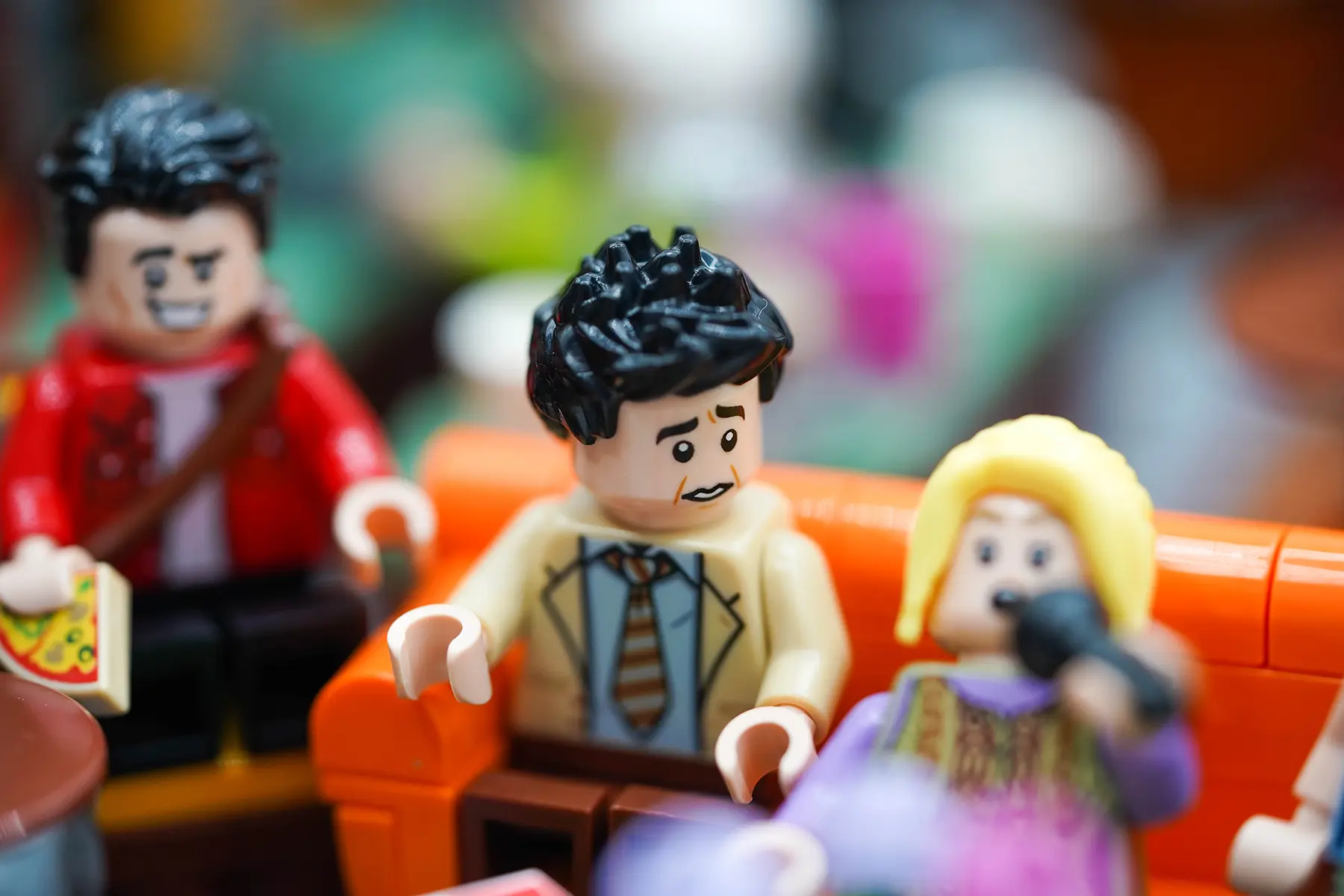 LEGO Joey and Phoebe on the iconic orange couch; Joey looks concerned while Phoebe sings into the mic.