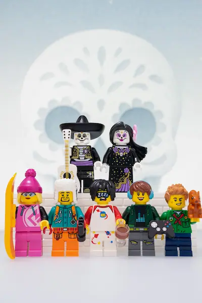 LEGO BAM October 2025 scene featuring Batman and the Bat-Family leaping above Harley Quinn and a group of escaped Arkham inmates, with flames and the asylum silhouetted in the background.