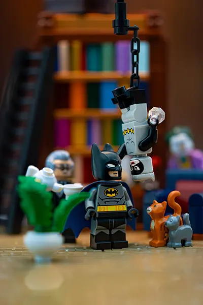 LEGO Batman confronts an upside-down Catwoman hanging from a chain in a library with Alfred and Joker in the background.