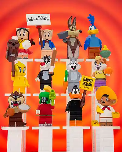 A lineup of LEGO Looney Tunes minifigures including Bugs Bunny, Daffy Duck, Porky Pig, Tweety, Sylvester, Road Runner, Wile E. Coyote, and others, posed together in a colorful cartoon-inspired setting.