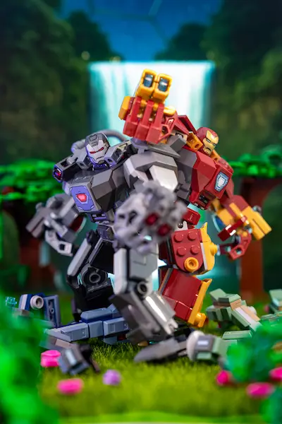 LEGO Iron Man and War Machine mechs pose back-to-back on a grassy base with a blurred waterfall backdrop.