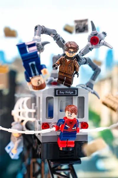 LEGO Spider-Man stops a runaway train as Doc Ock attacks from above in a dramatic city scene.