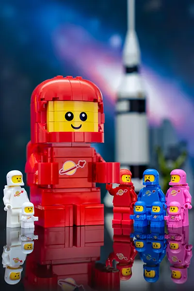 A large brick-built red classic space minifigure standing with smaller LEGO space minifigures in various colors