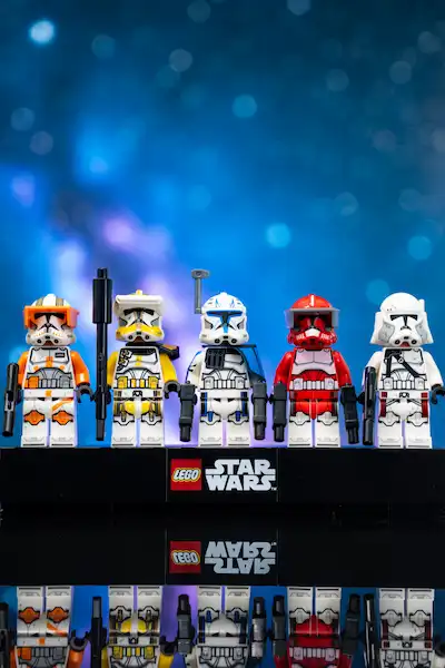 Five LEGO Star Wars clone commander minifigures in orange, yellow, blue, red, and white armor standing on a black base with a LEGO Star Wars logo and reflections below.