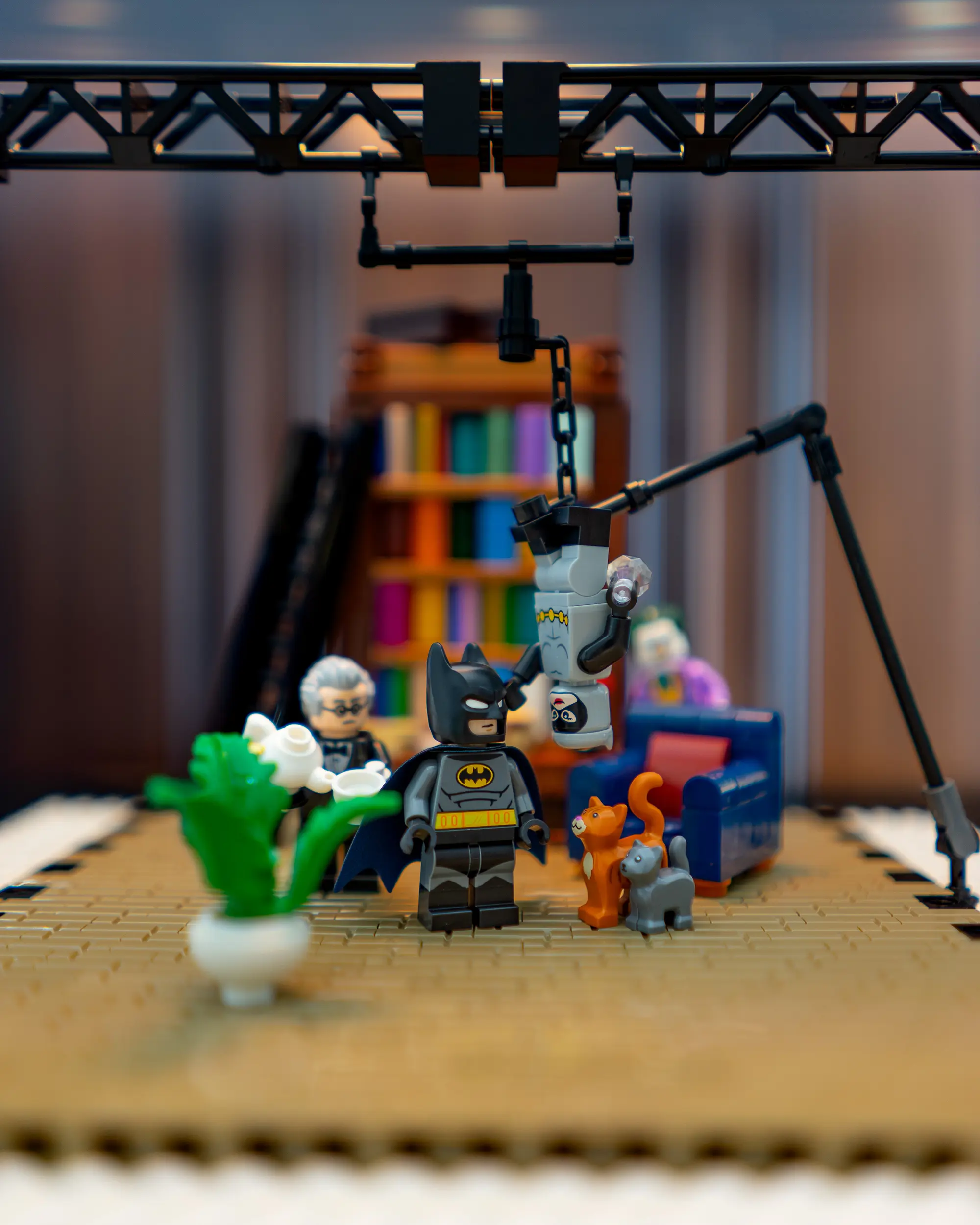 LEGO Batman on set with Alfred, Joker, and two cats, surrounded by studio rigging and props for a cozy interior scene.
