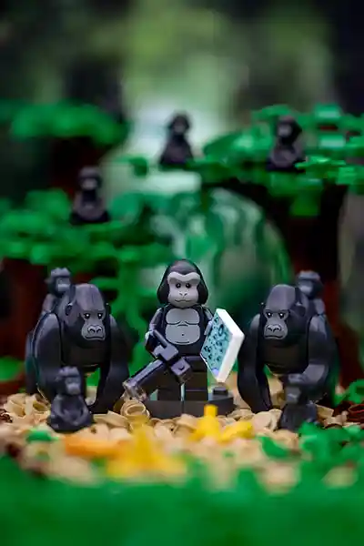 LEGO minifigure in a gorilla suit holding a camera and a map, surrounded by brick-built gorillas and banana pieces in a jungle setting.