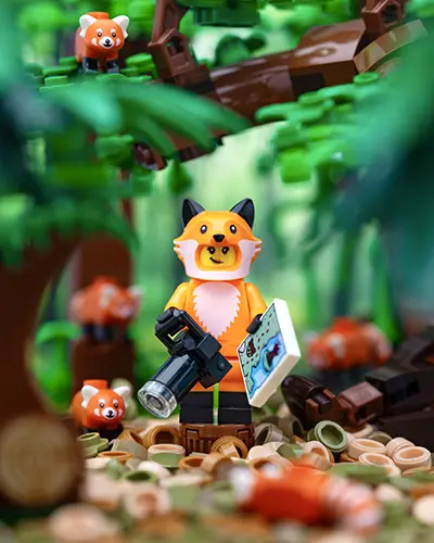 LEGO minifigure in a fox costume holds a camera and map, surrounded by red pandas in a lush LEGO forest.