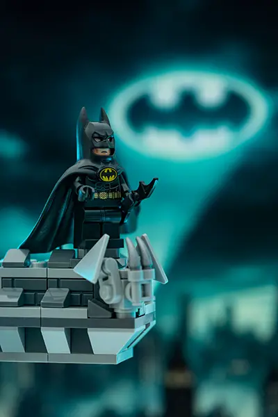LEGO Batman minifigure stands on a Gotham rooftop as the Bat-Signal glows behind him in the night sky.