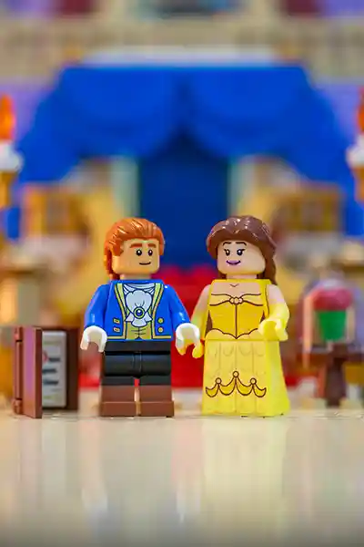 LEGO minifigures of Belle and the Beast in ballroom attire, standing in a castle-themed scene.
