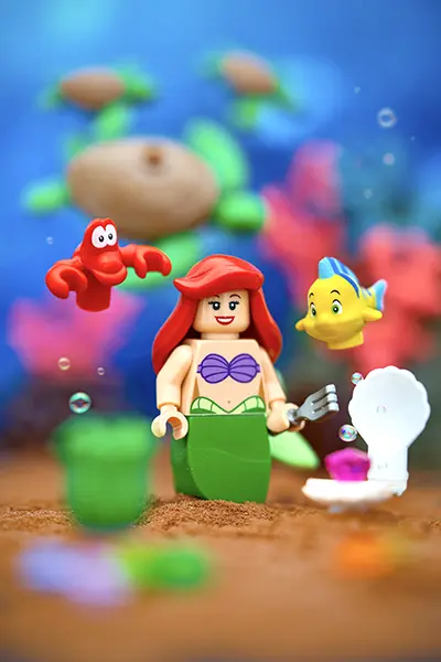 LEGO Ariel stands underwater holding a fork, surrounded by Flounder, Sebastian, and sea life treasures including a seashell and jewel.