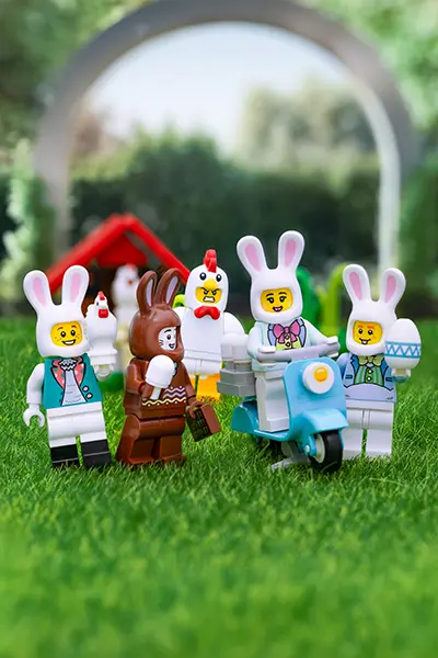 LEGO bunny-suited minifigures enjoy ice cream and ride a scooter on green grass with a chicken-suited figure and hen house in the background.
