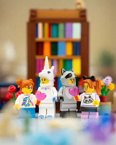 Four LEGO minifigures with animal-themed outfits holding pink hearts in a cozy room with flowers.