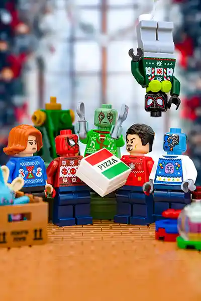 LEGO Marvel minifigures in Christmas sweaters enjoying a pizza party surrounded by festive decor.