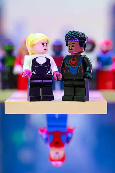 LEGO minifigures of Miles Morales and Gwen Stacy standing side by side with a reflection of Spider-Man hanging upside down beneath them.