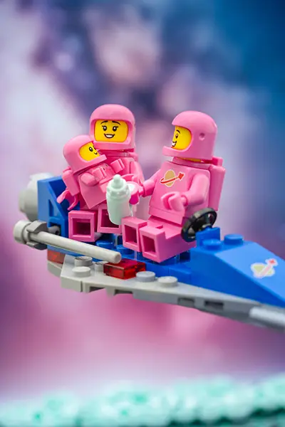 A LEGO space family in matching pink spacesuits rides a blue spaceship, feeding their baby in space.