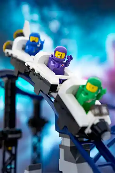 A thrilling LEGO space rollercoaster zooms through a cosmic landscape, with astronaut minifigures riding in colorful cars past planets, stars, and alien spectators.