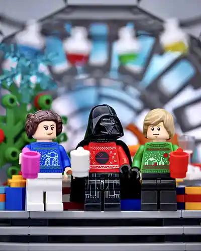 LEGO versions of Vader, Leia, and Luke enjoying holiday cheer with festive jumpers and hot drinks.